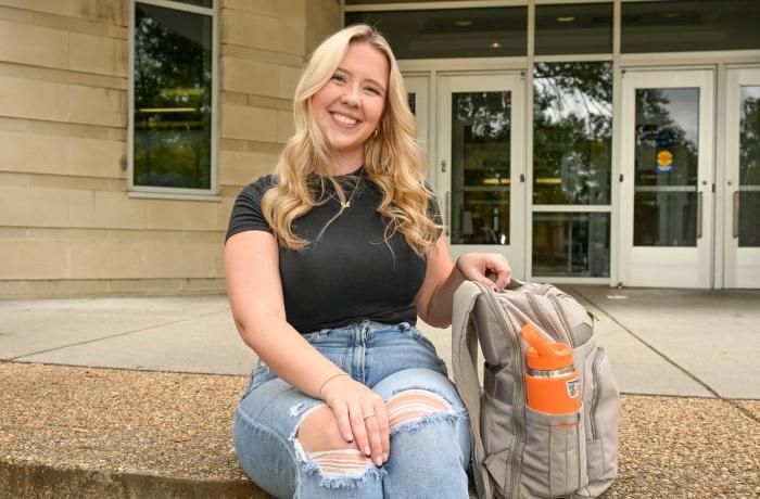 A woman sits on some steps in front of a building on ODU's campus. 